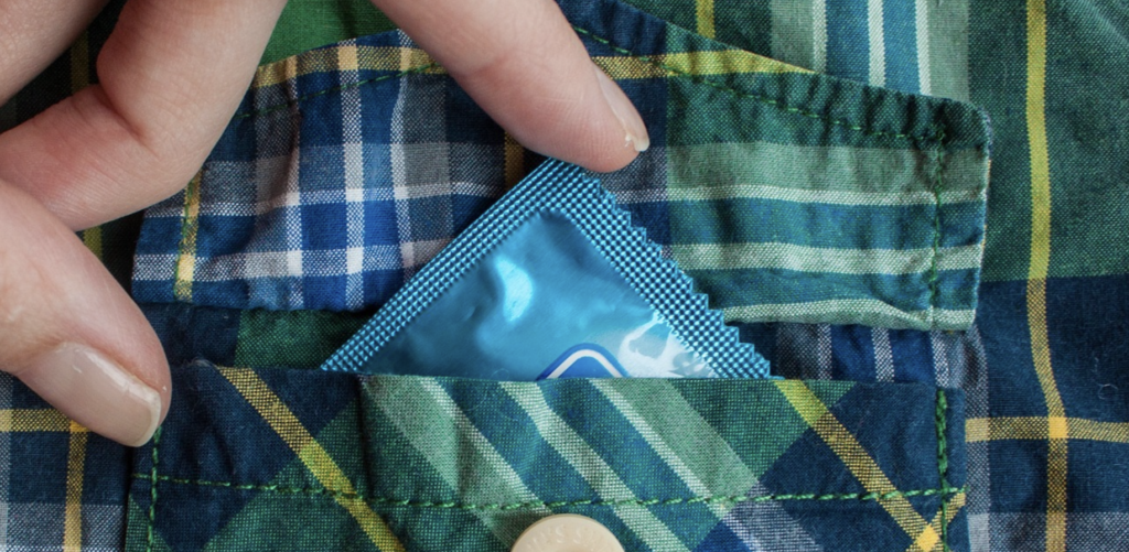 Mão feminina colocando camisinha dentro de bolso de camisa