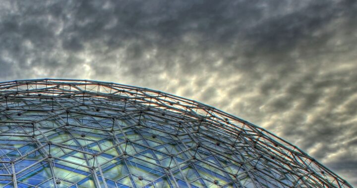 Foto en colores de invernadero de vidrio. Detrás de ella, nubes oscuras.