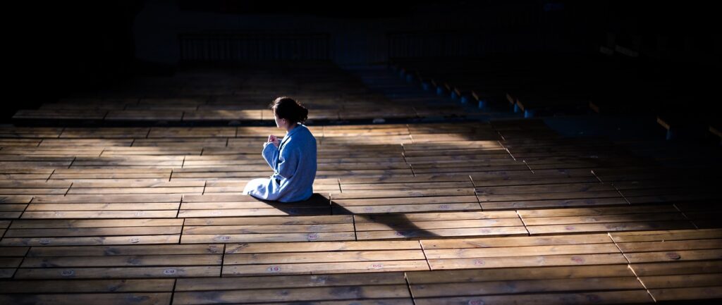 Fotografía en color de escenario de madera. En el centro, bajo el reflector, una mujer de pelo negro y pijama azul.