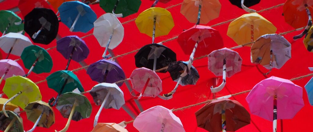 Fotografía en color de pequeñas sombrillas de papel de colores bajo un toldo rojo.