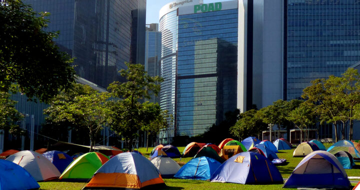 Fotografia em cores de barracas em gramado ao lado do Conselho Legislativo de Hong Kong. Imagem representa os protestos Occupy Central, de 2014.