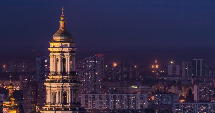 Fotografia em cores de panorama da cidade de Kiev, capital da Ucrânia, de noite. Em primeiro plano, vê-se o Mosteiro de Kiev-Petchersk. Ao fundo, prédios iluminados.