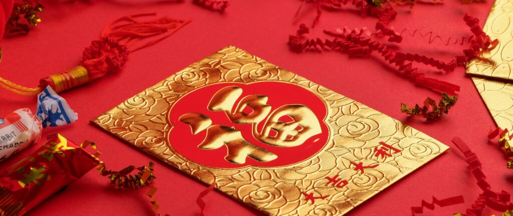 Fotografia em cores de envelope chinês vermelho e dourado. Ele está em uma superfície vermelha, cercado de enfeites vermelhos e dourados e doces chineses.