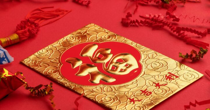 Fotografia em cores de envelope chinês vermelho e dourado. Ele está em uma superfície vermelha, cercado de enfeites vermelhos e dourados e doces chineses.