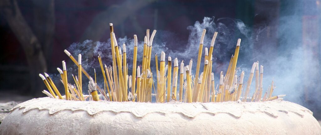 Fotografia em cores de incensos amarelos queimando dentro de vaso de concreto.