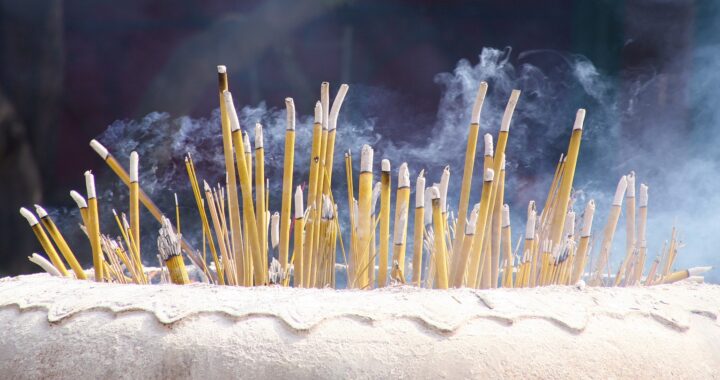 Fotografia em cores de incensos amarelos queimando dentro de vaso de concreto.