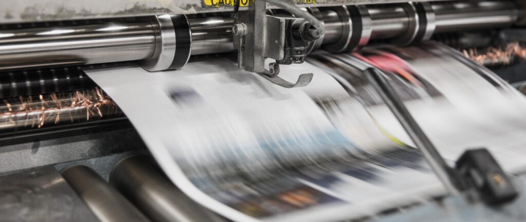 Fotografía en color de una página de periódico saliendo de la impresora.