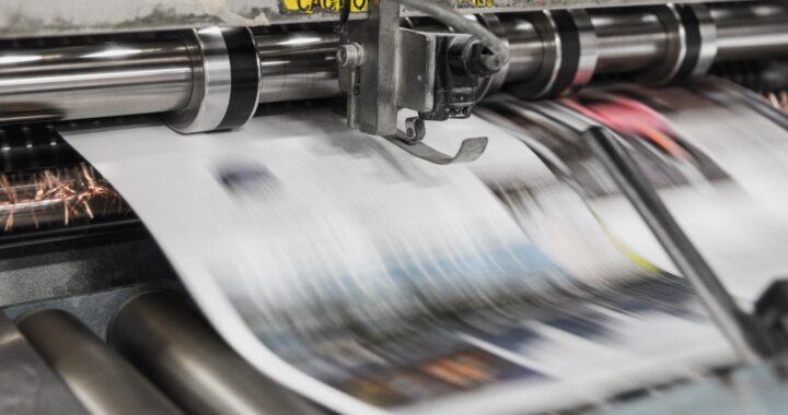 Fotografía en color de una página de periódico saliendo de la impresora.