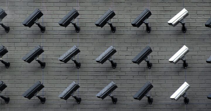 Fotografia de diversas câmeras de segurança, algumas pretas, outras brancas, em uma parede. Todas estão viradas para a mesma direção, esquerda abaixo.