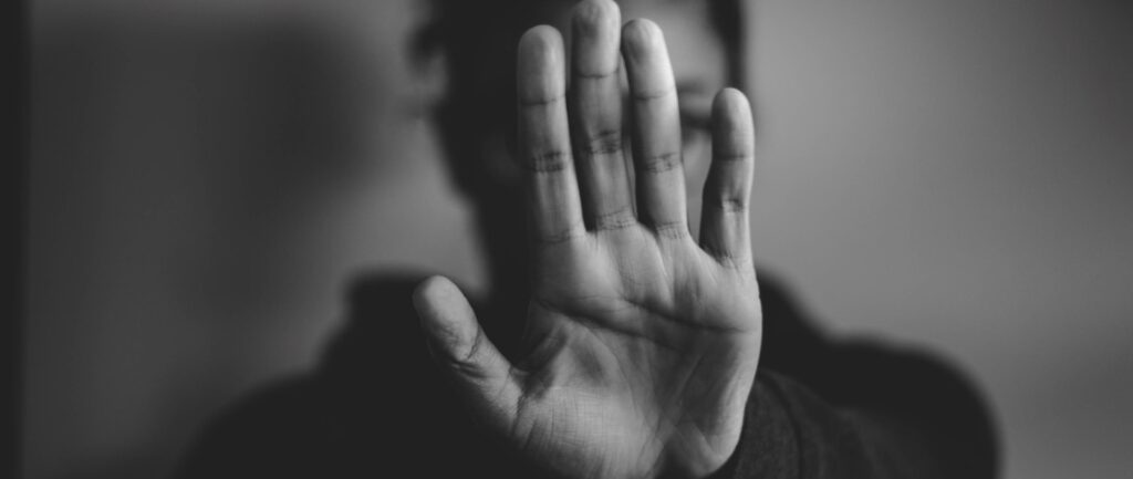 Fotografia em branco e preto de mulher. Sua mão esquerda está aberta, palma virada para a câmera, escondendo seu rosto.