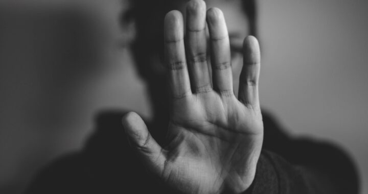 Fotografia em branco e preto de mulher. Sua mão esquerda está aberta, palma virada para a câmera, escondendo seu rosto.