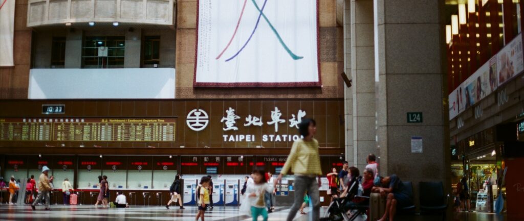 Fotografia em cores de pessoas circulando pela Taiwan Station, em Taipei.