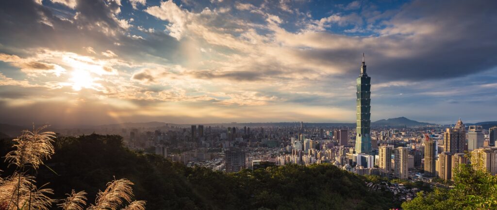 Fotografia em cores de panorama de Taipei em dia de sol e nuvens. Em destaque, o prédio 101.