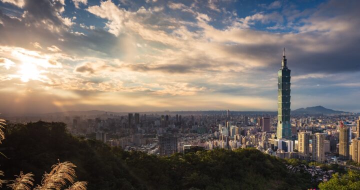 Fotografia em cores de panorama de Taipei em dia de sol e nuvens. Em destaque, o prédio 101.