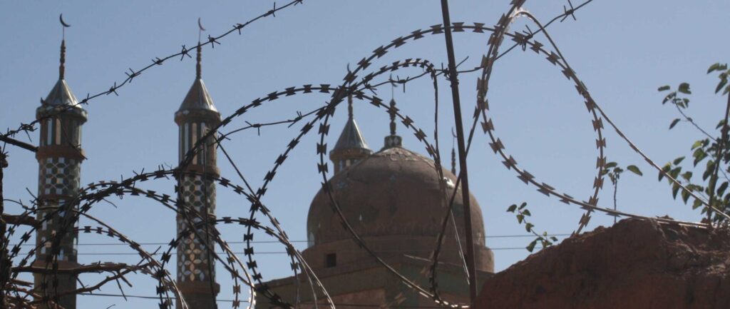 Fotografia em cores de mesquita em Xinjiang vista através de arames farpados.