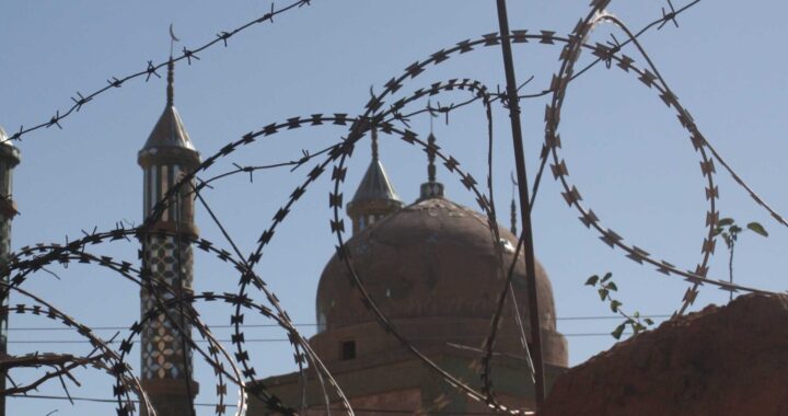 Fotografia em cores de mesquita em Xinjiang vista através de arames farpados.