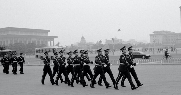 Fotografia em preto e branco, contemporânea, de soldados marchando uniformizados na Praça da Paz Celestial.
