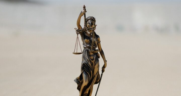 Fotografia em cores de estátua representando a justiça - uma mulher de olhos vendados segurando uma balança com dois pratos equilibrados.