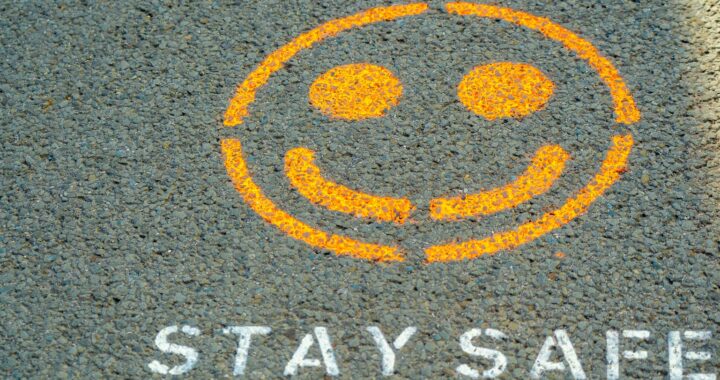 Fotografia em cores de grafitti no asfalto: um rosto amarelo, sorrindo, e a mensagem stay safe.