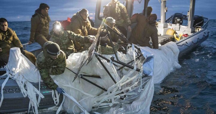 Fotografia em cores de marinha dos EUA resgatando o balão chinês no oceano. Pode-se ver marinheiros em um bote, no começo da noite, puxando o balão para dentro da embarcação.