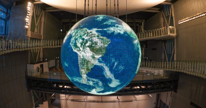 Fotografia em cores de globo iluminado, com a América Latina em primeiro plano. O globo é grande e pende do teto de um salão espaçoso.