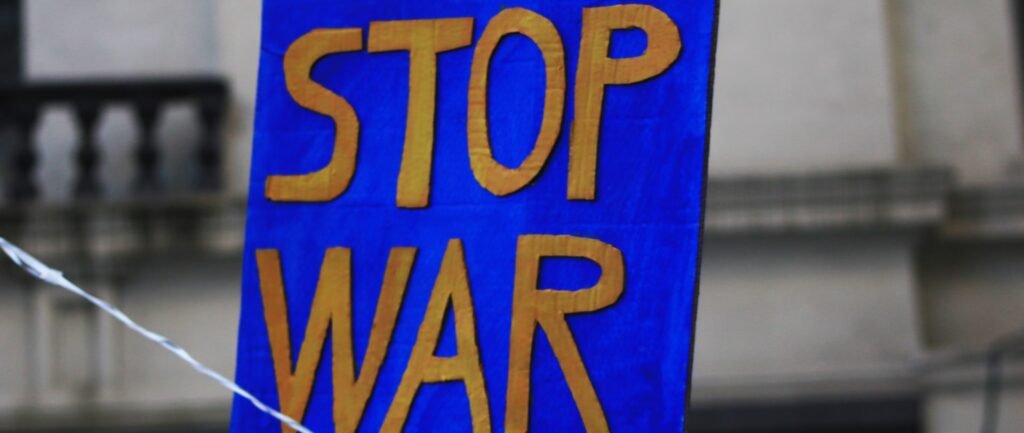Fotografia em cores de cartaz em azul, com as palavras STOP WAR (pare a guerra) escritas em amarelo.