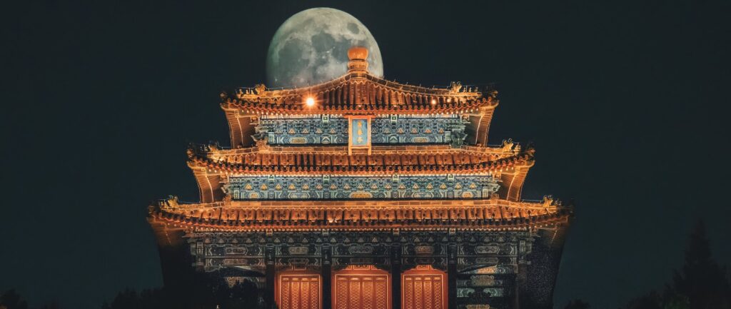 Fotografia em cores do Pavilhão Wanchun em Jingshan, Pequim. Ao fundo, sobre o telhado, vê-se a lua cheia.