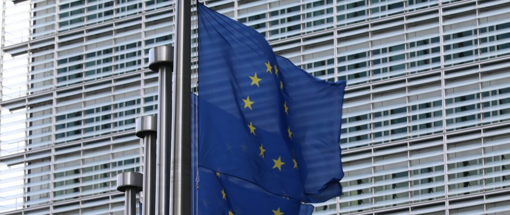 Fotografia em cores de uma sequência de bandeiras da União Europeia em frente a um prédio.