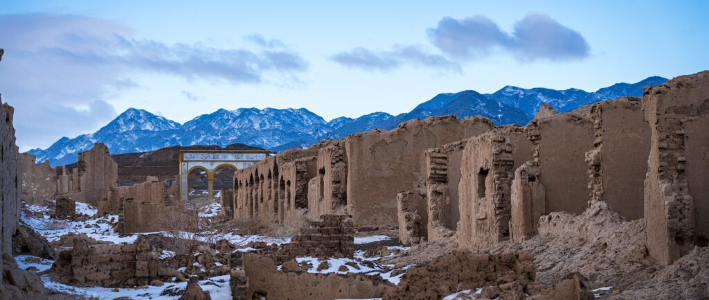 Uma estrada de terra com neve no chão e montanhas ao fundo.