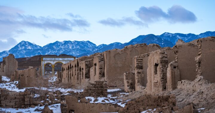 Uma estrada de terra com neve no chão e montanhas ao fundo.