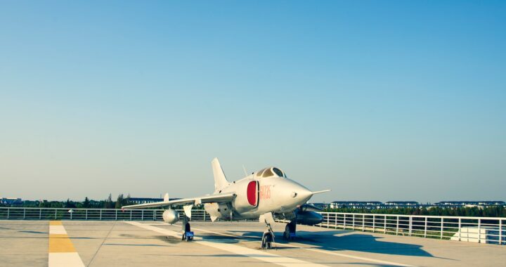 Fotografia em cores de jato militar estacionado em uma pista de pouso em dia de céu azul.