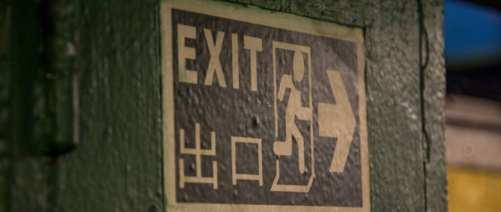 Fotografia em cores de placa verde e branca indicando saída em inglês e chinês.