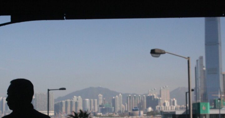 Foto da skyline de Hong Kong, em que a silhueta de um homem está em primeiro plano e ele olha para o lado.
