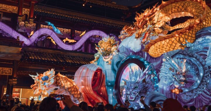 Fotografia em cores de apresentação em templo chinês assistida por um grupo de pessoas. Uma enorme lanterna de papel representa diferentes dragões chineses.