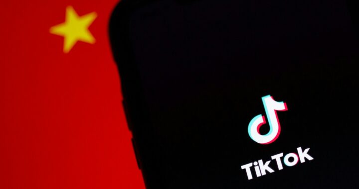 Fotografia em cores de celular na tela de carregamento do app TikTok. Ao fundo, a bandeira da China.