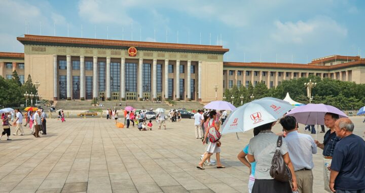 Fotografia em cores de pessoas com sombrinhas passeando pela Praça da Paz Celestial em dia de sol.