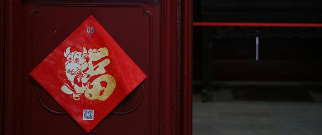 Fotografia em cores de porta de madeira com amuleto vermelho com caracter dourado para atrair boa fortuna.