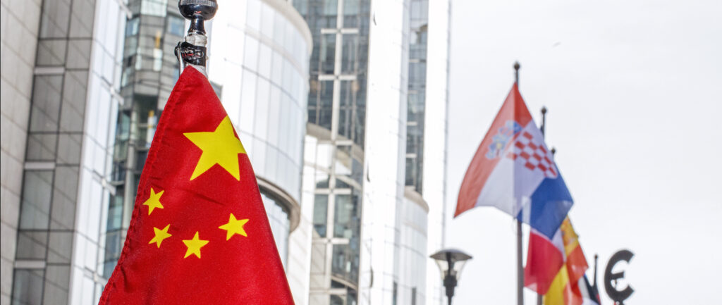 Foto de bandeiras no prédio do Parlamento Europeu, com a bandeira da China em primeiro plano e outras bandeiras europeias e o logo do Euro