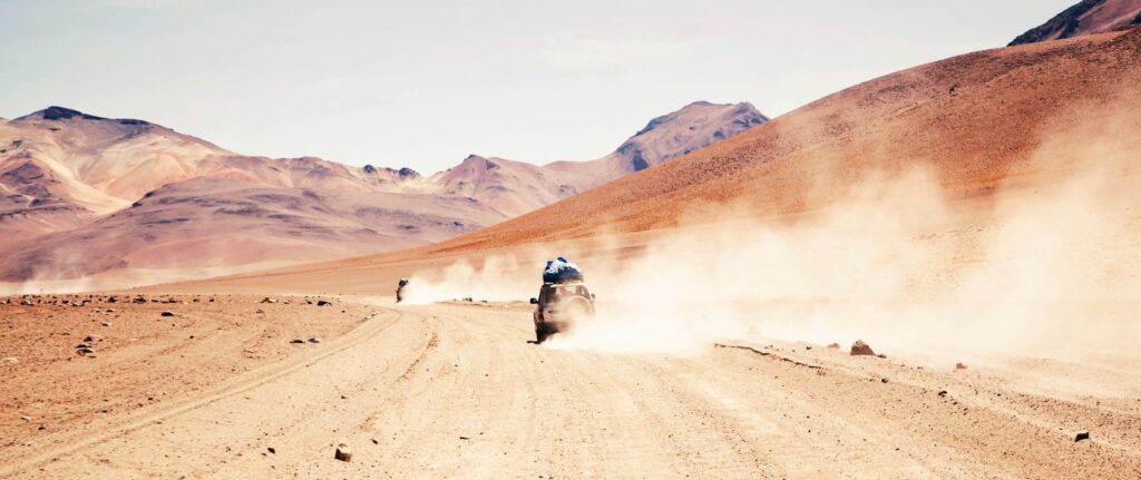 Fotografia em cores de jipe acelerando em deserto na Bolívia.