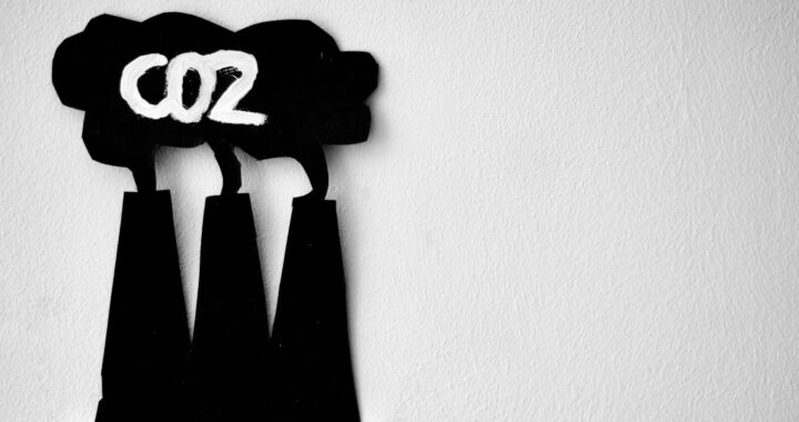 Imagem de recorte em material preto. O recorte tem a forma de três chaminés expelindo uma nuvem. Na nuvem está escrito, em branco, CO2.