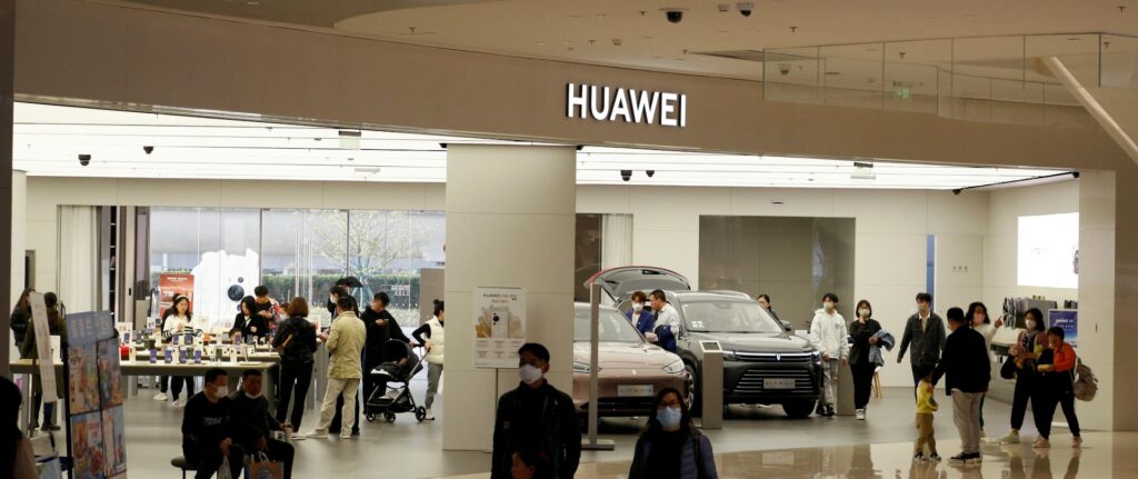 Um grupo de pessoas em um prédio amplo, com uma loja da Huawei ao fundo vendendo carros