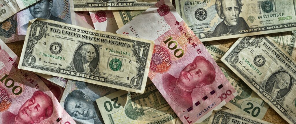 Fotografia em cores de notas de dólar estadunidense e renminbi chinês.