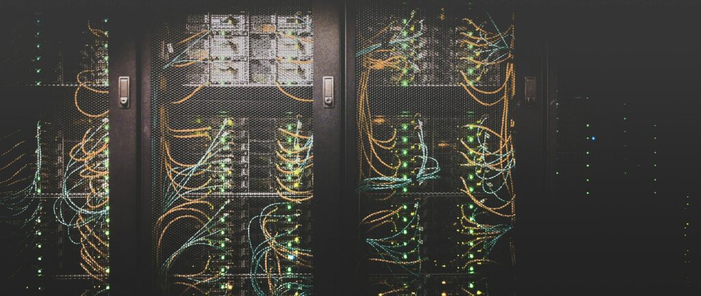 Fotografia em cores de um armário em um data center. Dentro dele, é possível ver cabos amarelos e verdes, além de leds acesos.