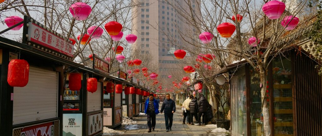 uma rua com decoração de ano novo lunar, dois pedestres caminham, barracas estão fechadas