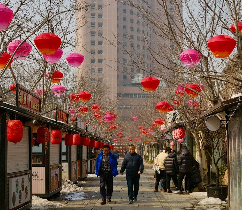 uma rua com decoração de ano novo lunar, dois pedestres caminham, barracas estão fechadas