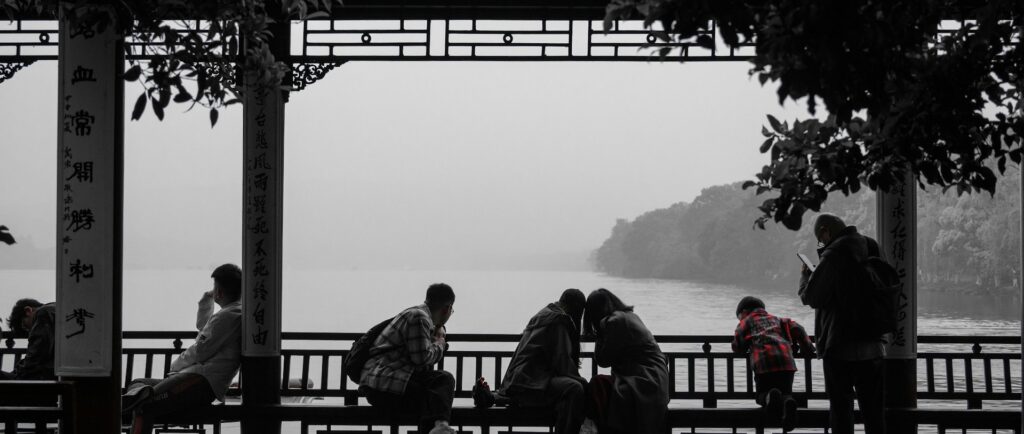 Fotografia, a maior parte dela em branco e preto, de pessoas em uma bela varanda com arabescos chineses com vista para um rio – no entanto, nota-se o vermelho da camisa de um menino.