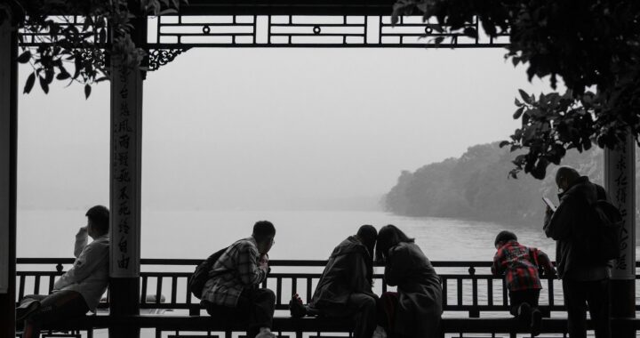 Fotografia, a maior parte dela em branco e preto, de pessoas em uma bela varanda com arabescos chineses com vista para um rio – no entanto, nota-se o vermelho da camisa de um menino.