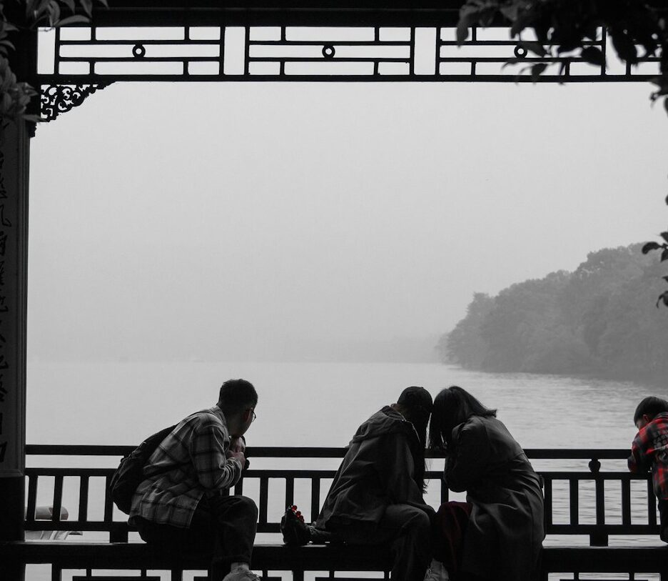 Fotografia, a maior parte dela em branco e preto, de pessoas em uma bela varanda com arabescos chineses com vista para um rio – no entanto, nota-se o vermelho da camisa de um menino.
