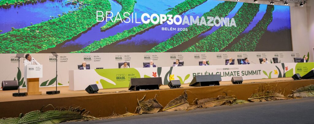Fotografia da abertura da Plenária da COP30, com uma mesa branca e um painel grande ao fundo dizendo Brasil COP30 Amazônia