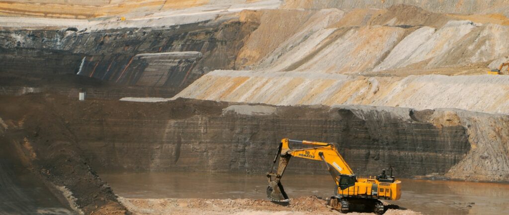 Fotografia em cores de escavadora amarela em sítio de mineração.